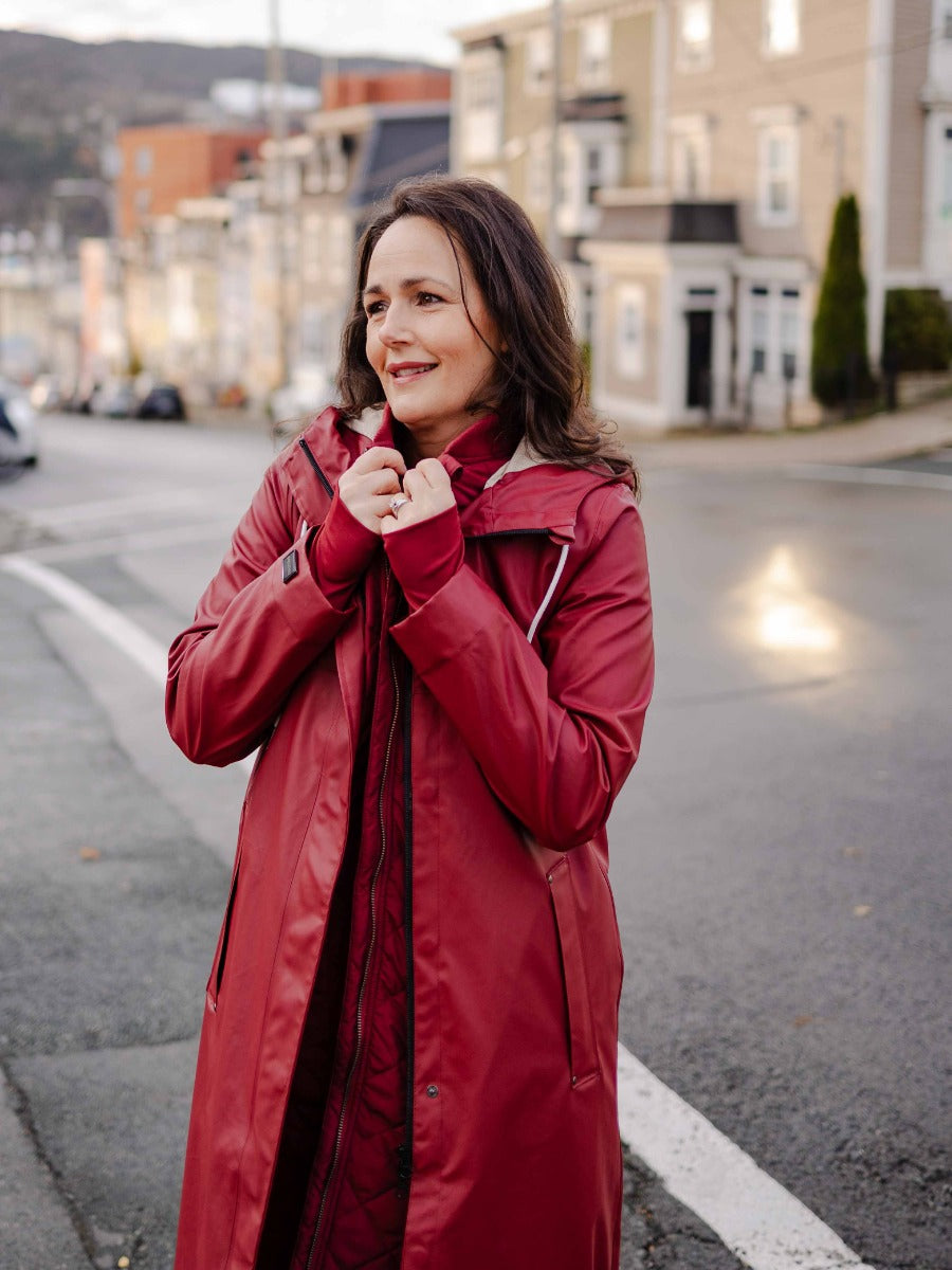 Person outdoors wearing a long red coat over a quilted jacket, standing on a quiet residential street.