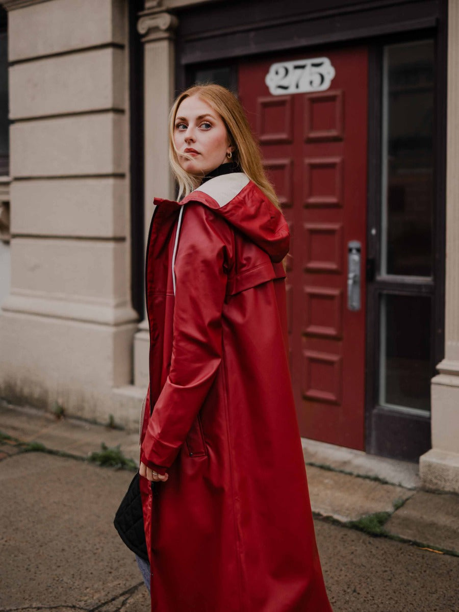 Person in a long red coat with a hood standing on a sidewalk near a building with a maroon door numbered 275.
