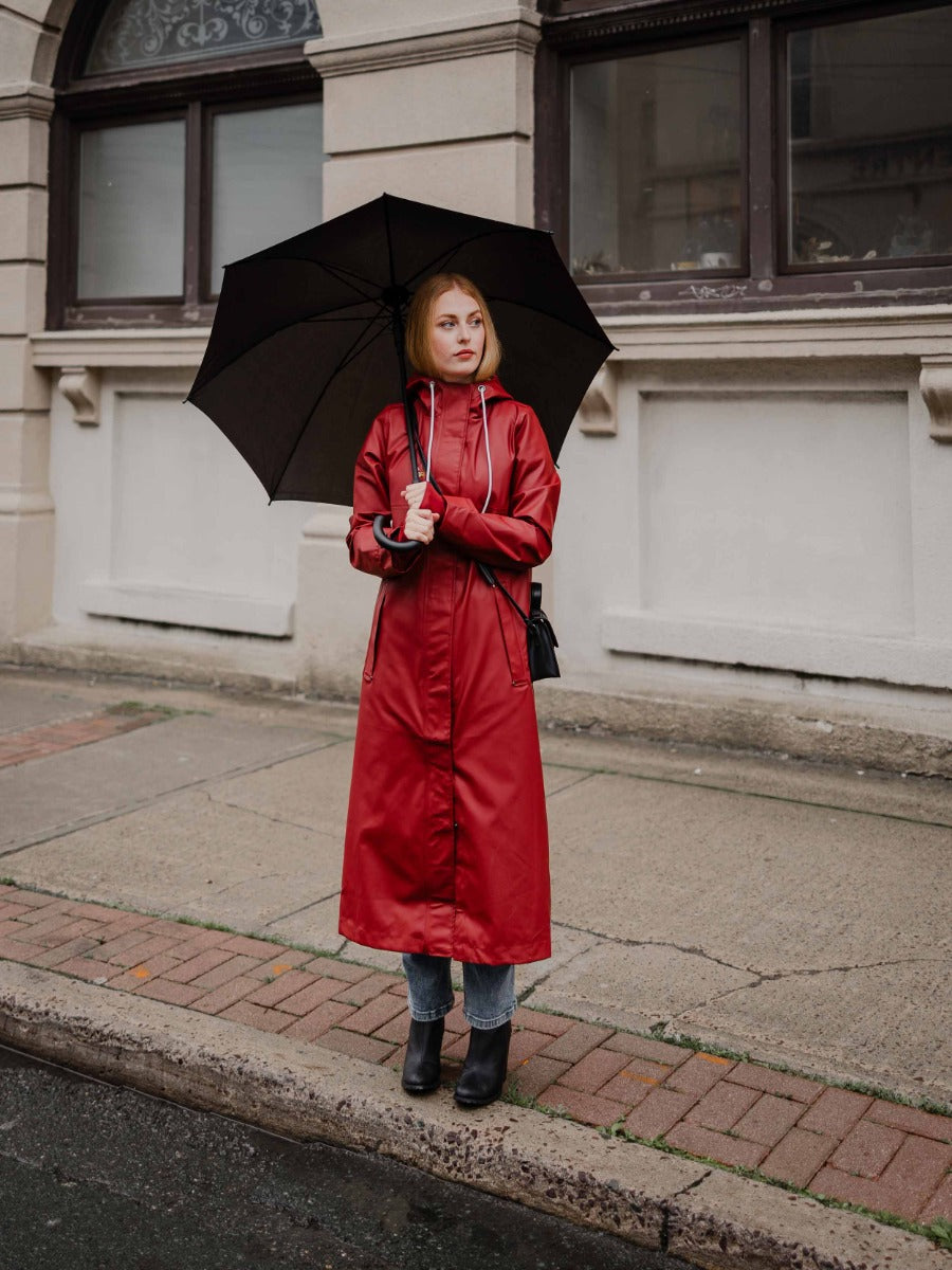 Red waterproof long raincoat with hood holding black umbrella outdoors, Mernini Petite 42” Length Waterproof Raincoat by MERNINI/ROCK RAIN INC.