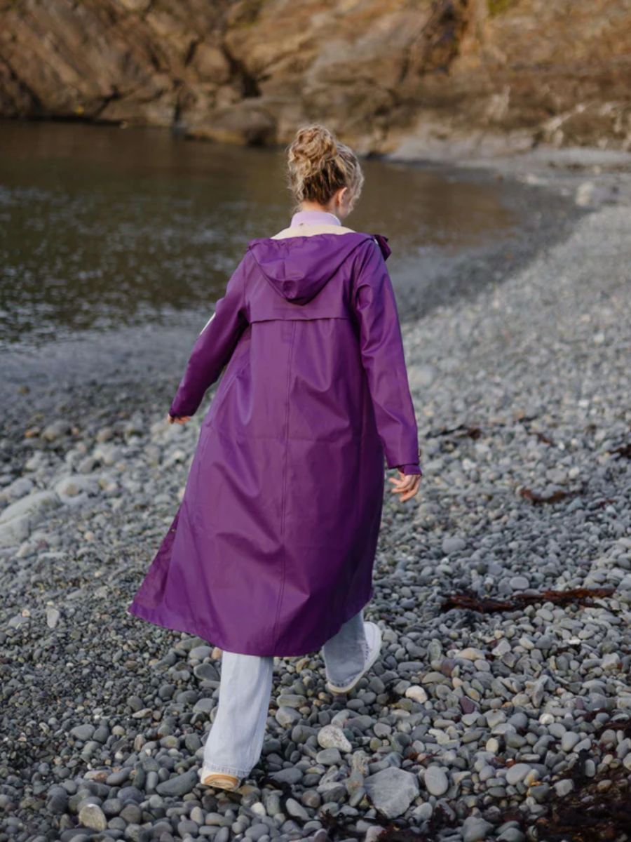 Long purple raincoat with a hood worn outdoors on a rocky shoreline near water and cliffs.