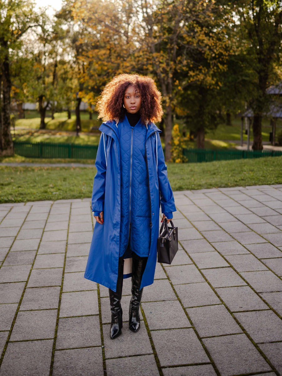 Model outdoors wearing a blue Mernini Petite 42” Length Waterproof Raincoat by MERNINI/ROCK RAIN INC, styled with boots.