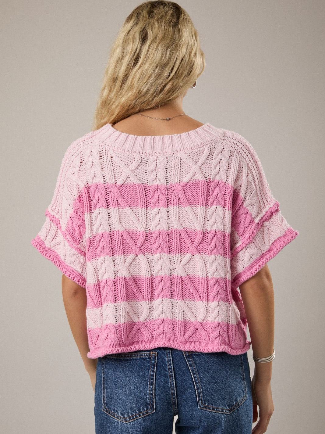 Light pink and dark pink striped knitted short-sleeve sweater with a cable pattern paired with blue denim jeans