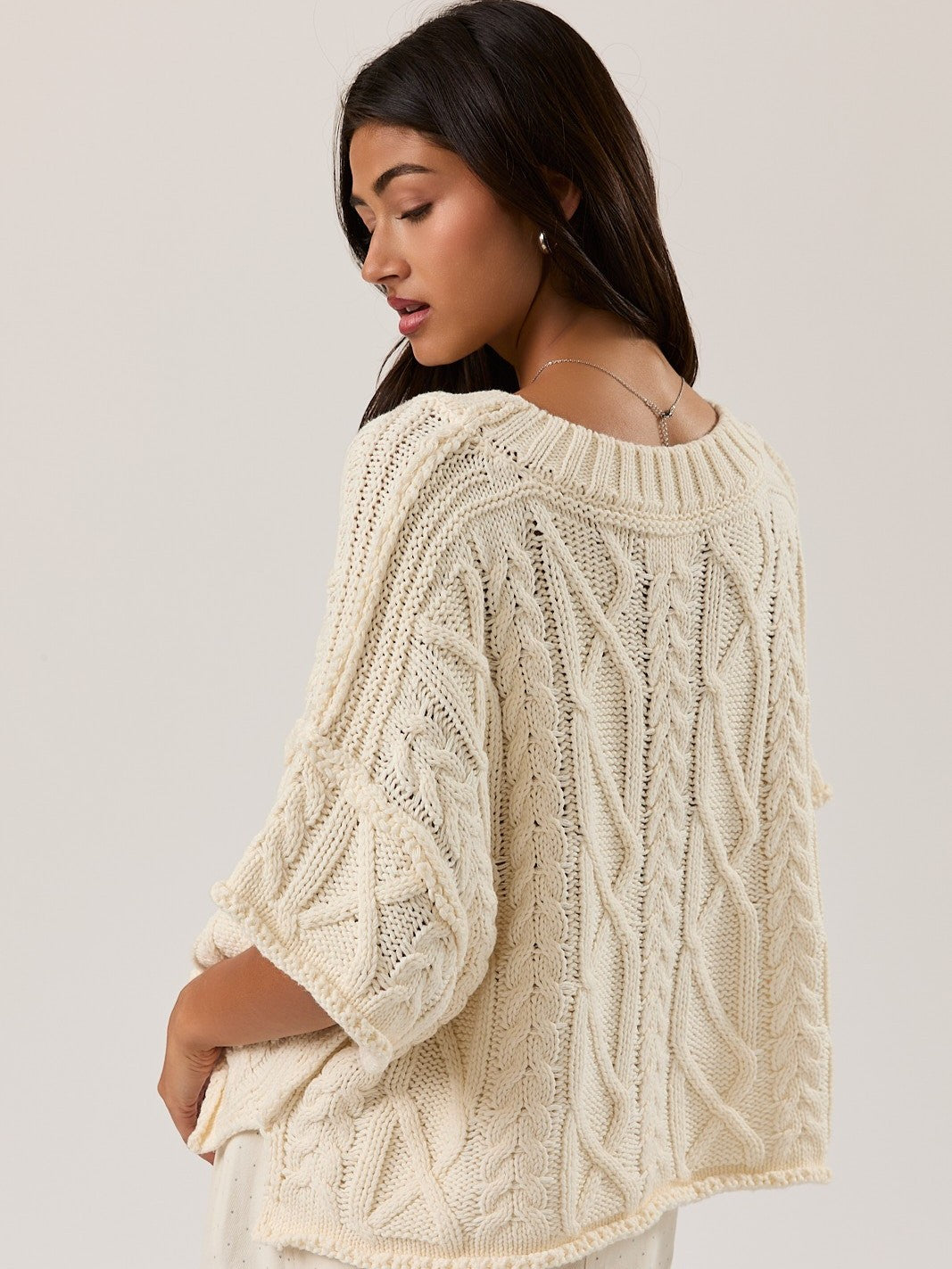 Cream-colored chunky cable knit sweater with wide sleeves and ribbed neckline, shown from the back side.