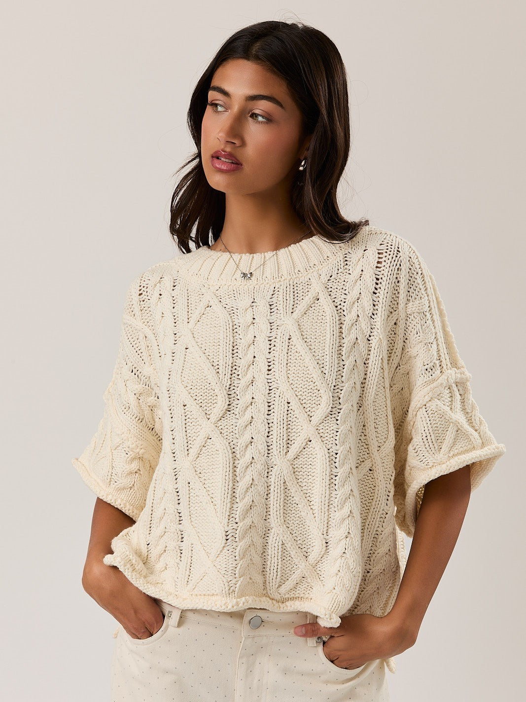 Cream cable knit Amy Cotton Blend Short Sleeve Crew Sweater by Le lis, styled with light pants, model looking sideways.
