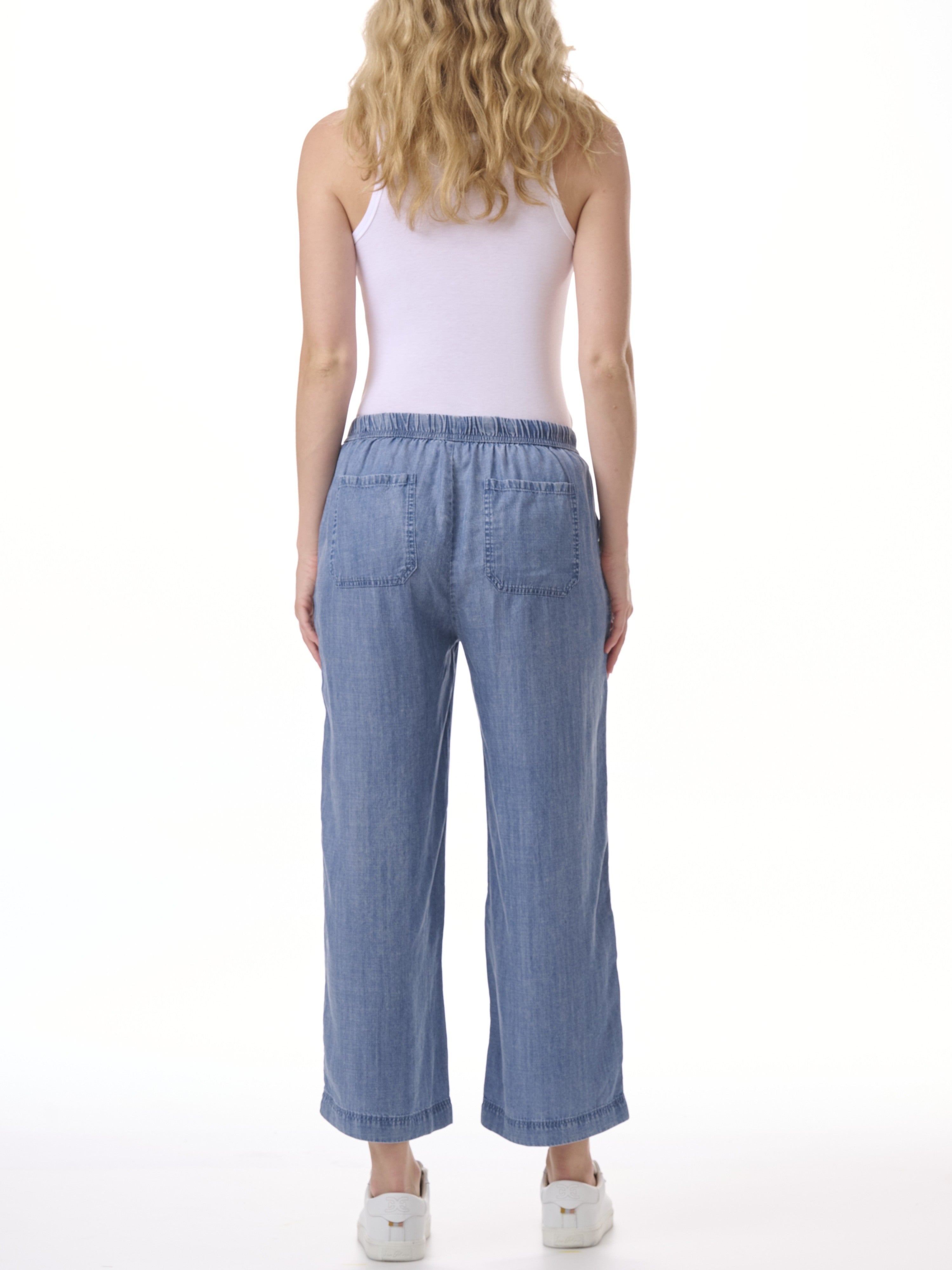 Back view of light blue denim wide-leg pants with elastic waistband and patch pockets paired with white sneakers.