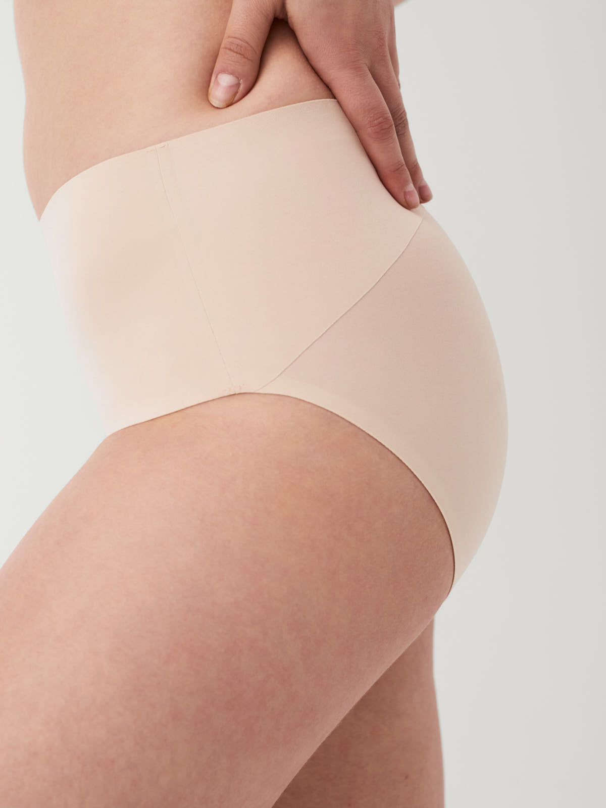 Close-up of neutral-toned seamless underwear on a person’s hip and thigh against a plain background.