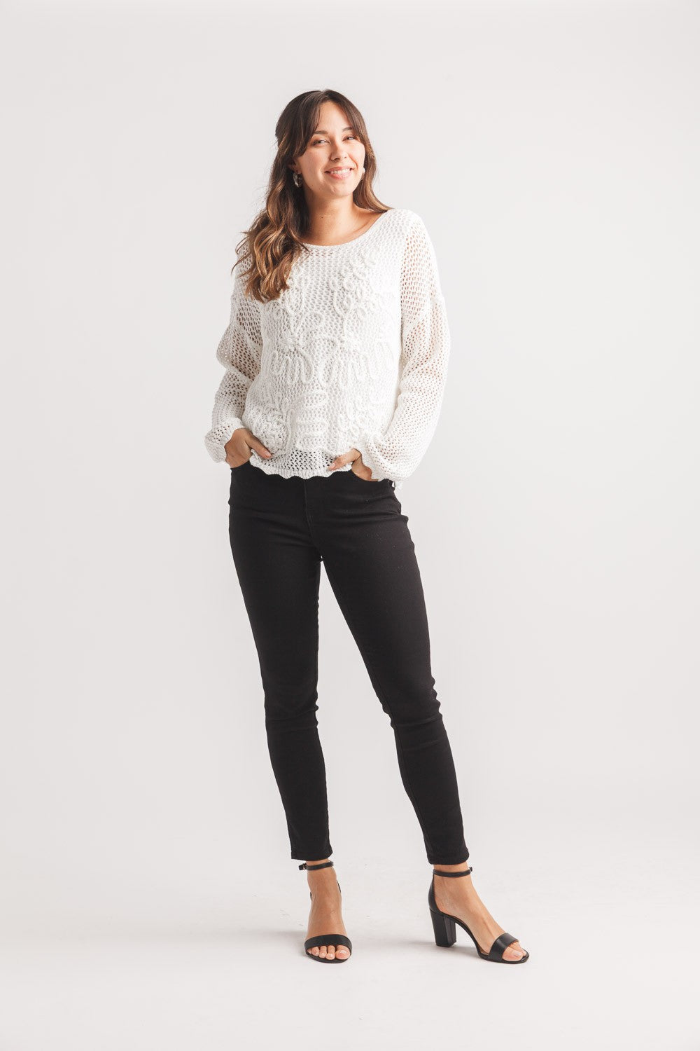 Model in black pants and sandals with Papillon Daisy Open Knit Crew Sweater in white by Papillon against a plain background