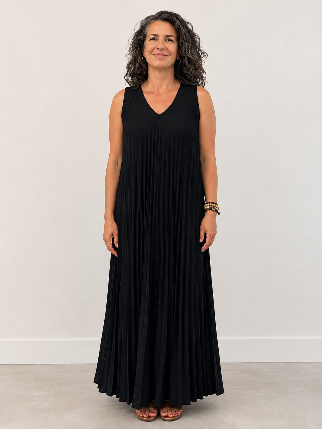 Accordion Pleated Sleeveless Maxi Dress by Plum Loco in black with V-neck and flowing pleated fabric reaching the floor.