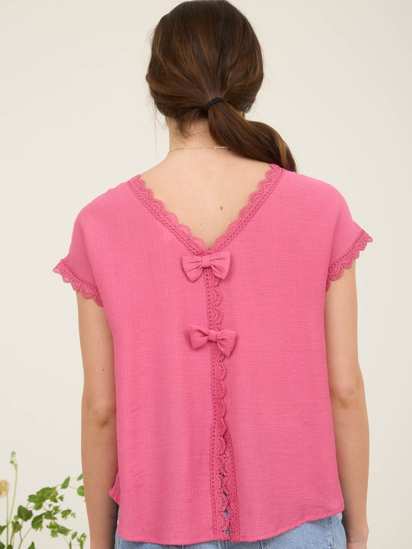 Back view of a fuchsia pink textured top with lace trim and two fabric bows on the back neckline and center seam.
