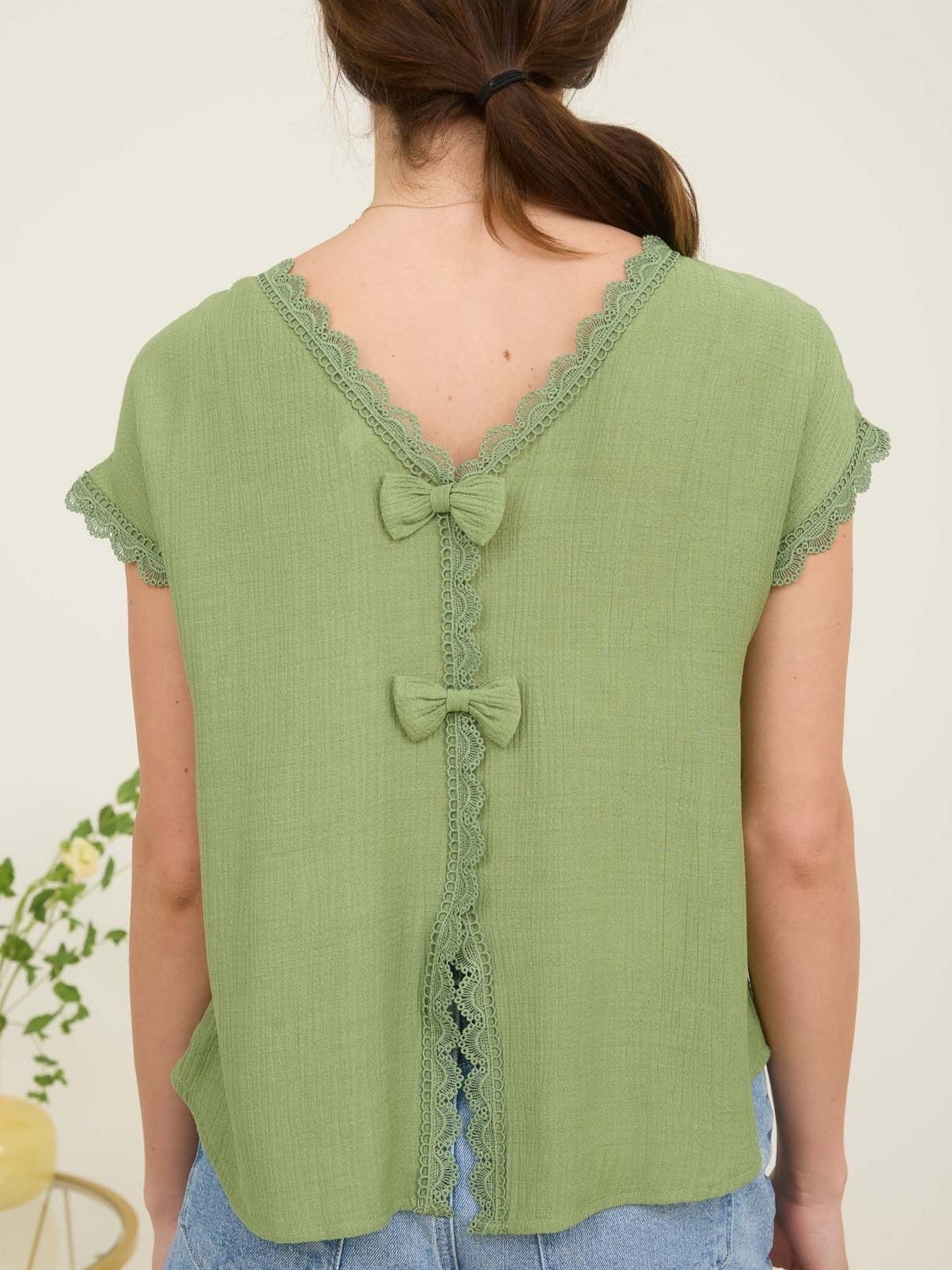 Light green textured top with lace trim and two decorative bows on the back, paired with blue denim bottoms.