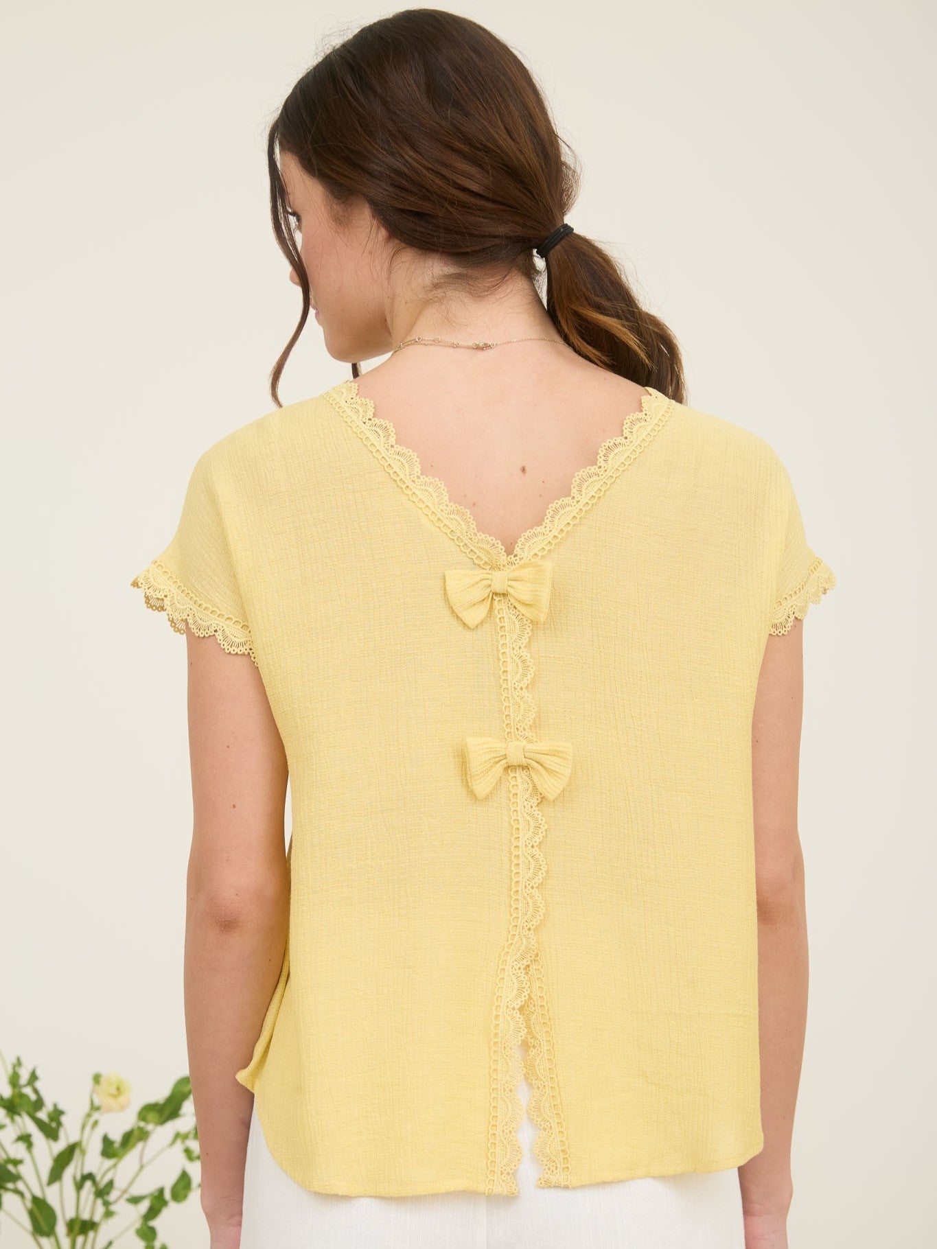 Yellow short-sleeve top with lace trim and two decorative bows on the back neckline and center seam