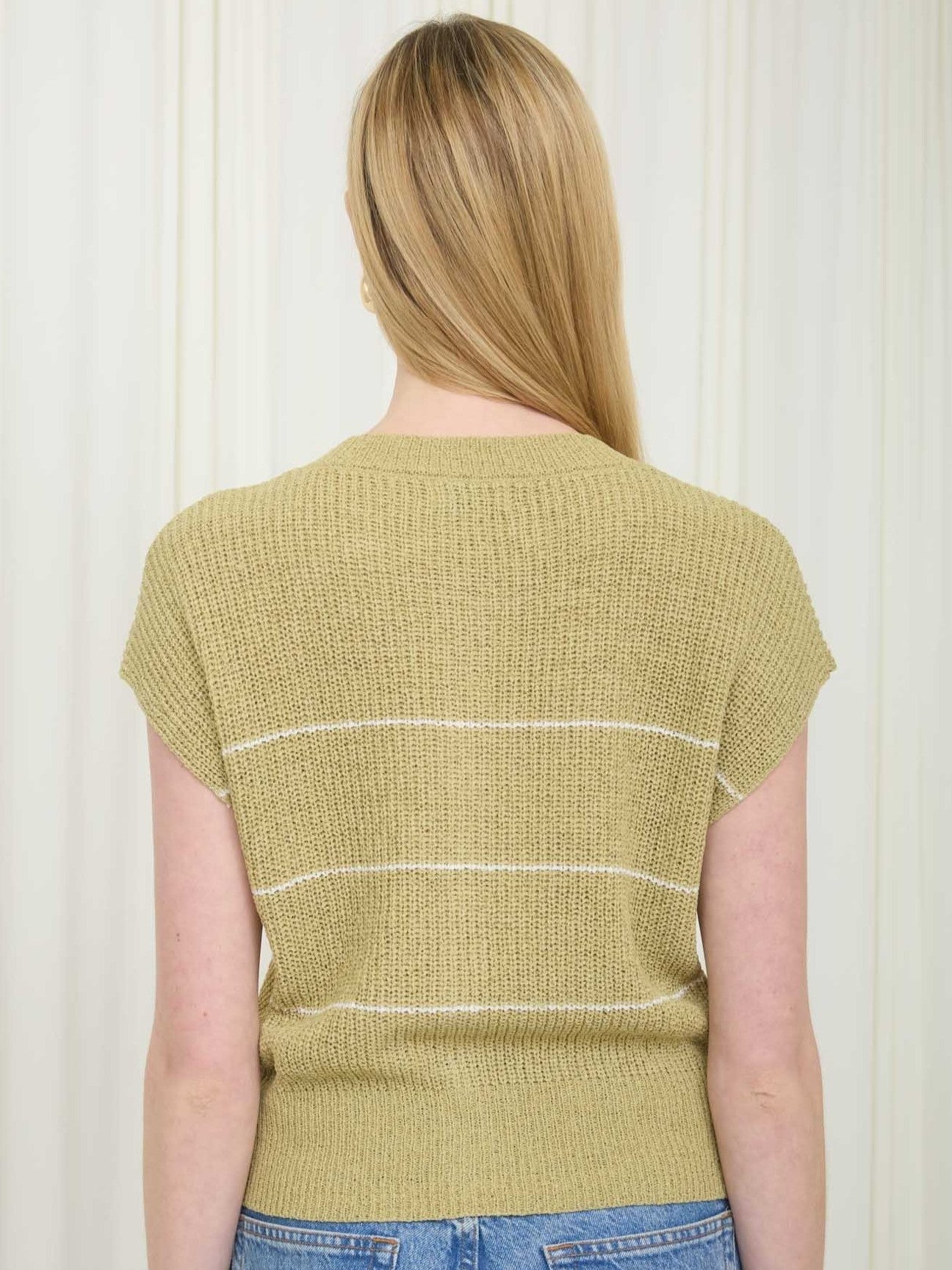 Back view of a sleeveless olive knit sweater with subtle horizontal stripes paired with blue denim jeans
