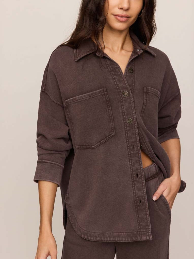 Close-up of a brown button-up shirt with two chest pockets and rolled-up sleeves on a neutral background.
