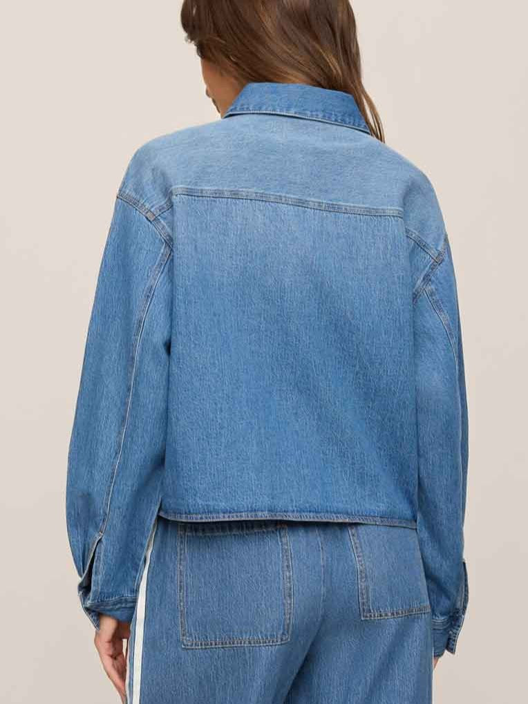 Back view of a light blue denim jacket paired with matching denim pants against a neutral background.