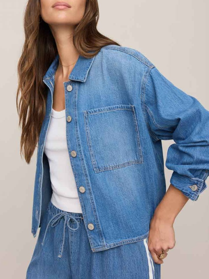 Light blue denim jacket with front pocket and button closure over a white top and matching denim pants with drawstring waist