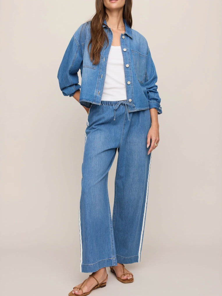 Blue denim jacket paired with matching wide-leg denim pants featuring white side stripes and tan sandals.