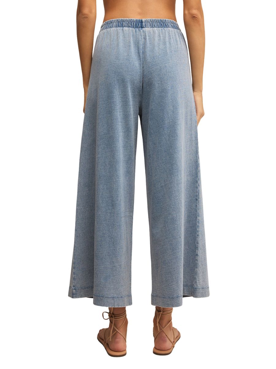 Back view of light blue wide-leg cropped denim pants with an elastic waistband and sandals.