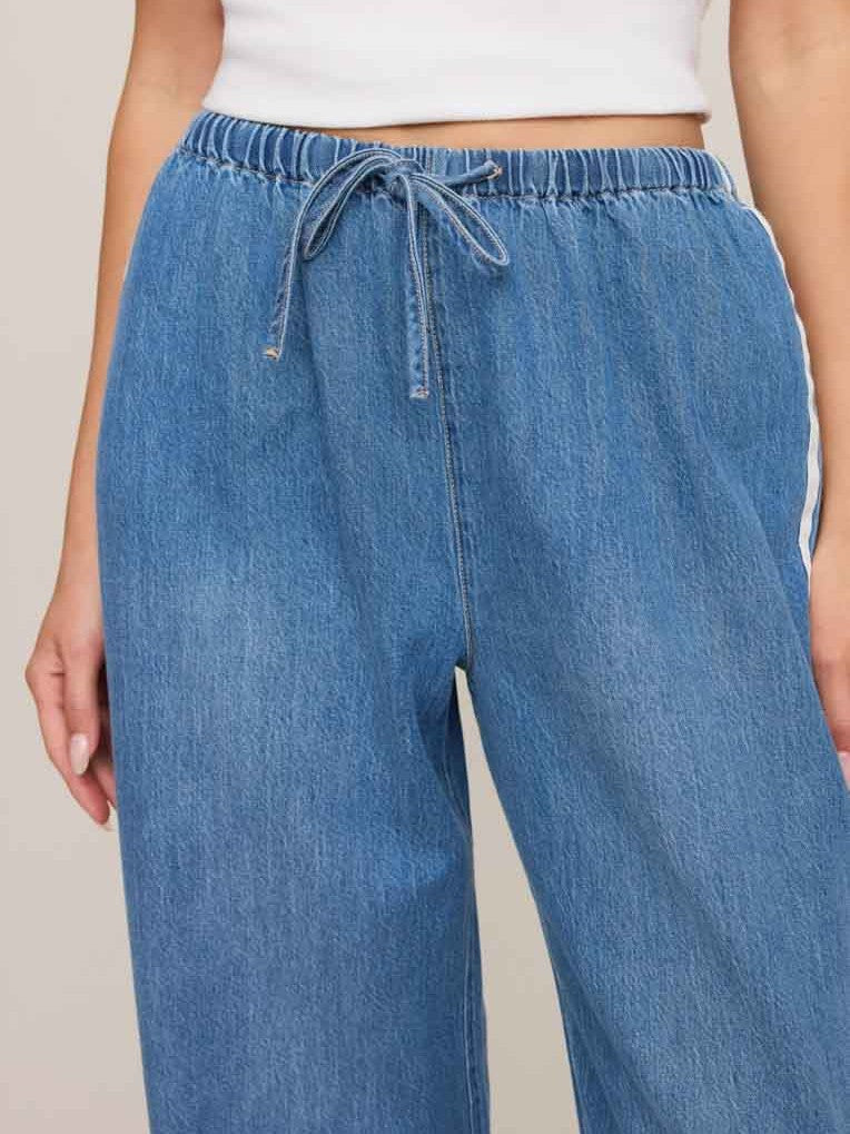 Blue denim pants with elastic waistband and drawstring tie, featuring a relaxed fit and side stripe detail.