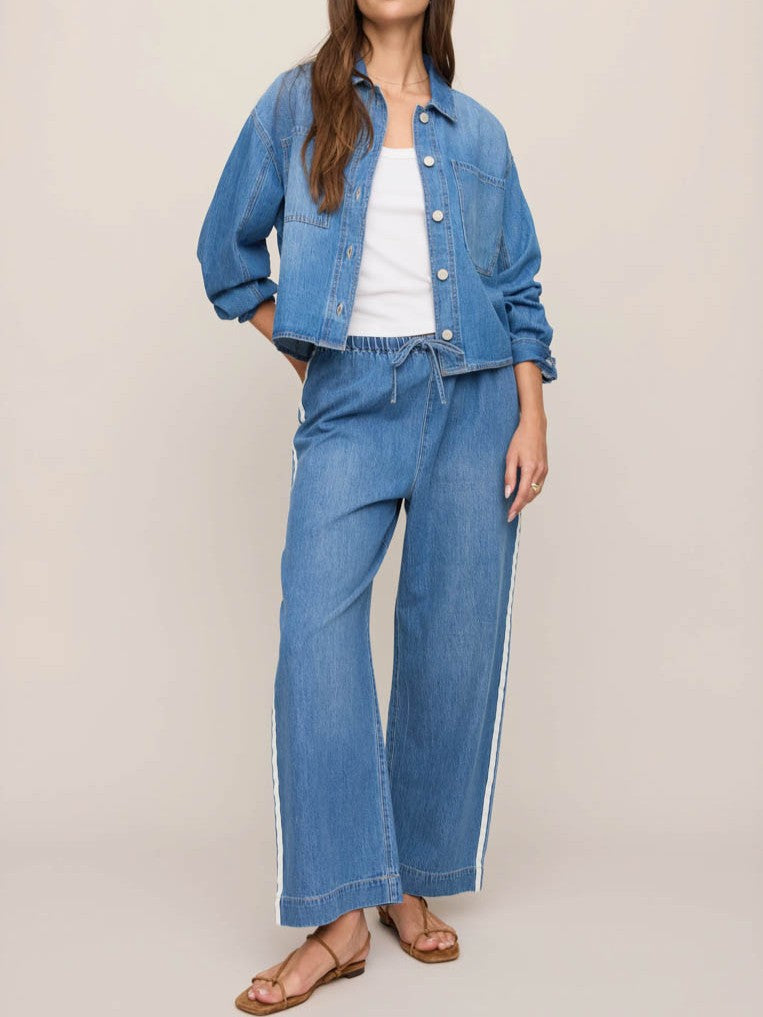 Denim jacket with buttons paired with matching wide-leg denim pants featuring side stripes and a white tank top.