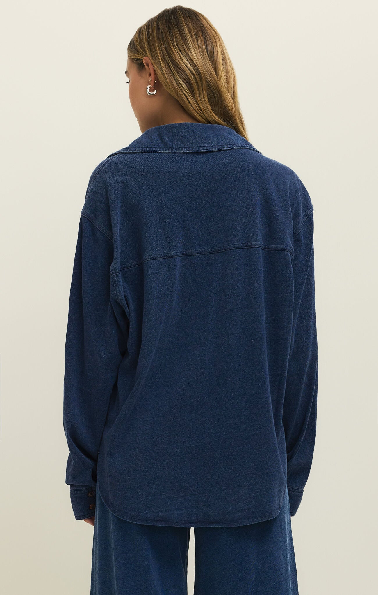 Back view of a person wearing a dark blue denim jacket and matching pants against a plain background