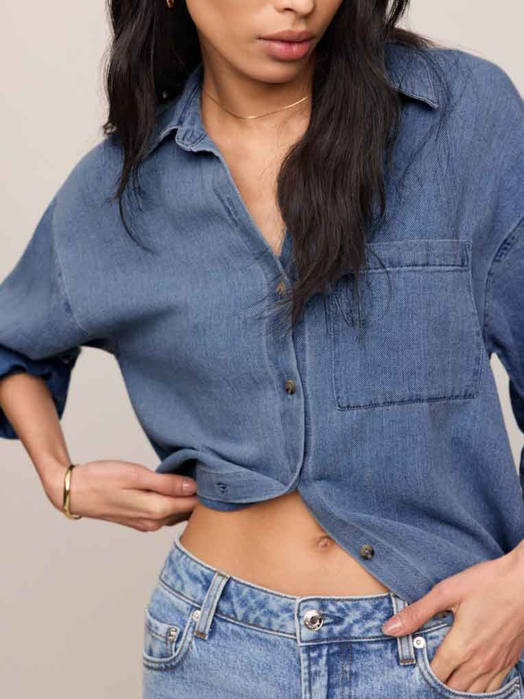Close-up of an indigo denim shirt with front pocket paired with light-wash denim jeans and gold jewelry accessories.