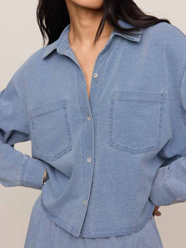 Close-up of a light blue denim jacket with front pockets and button closures on a neutral background.