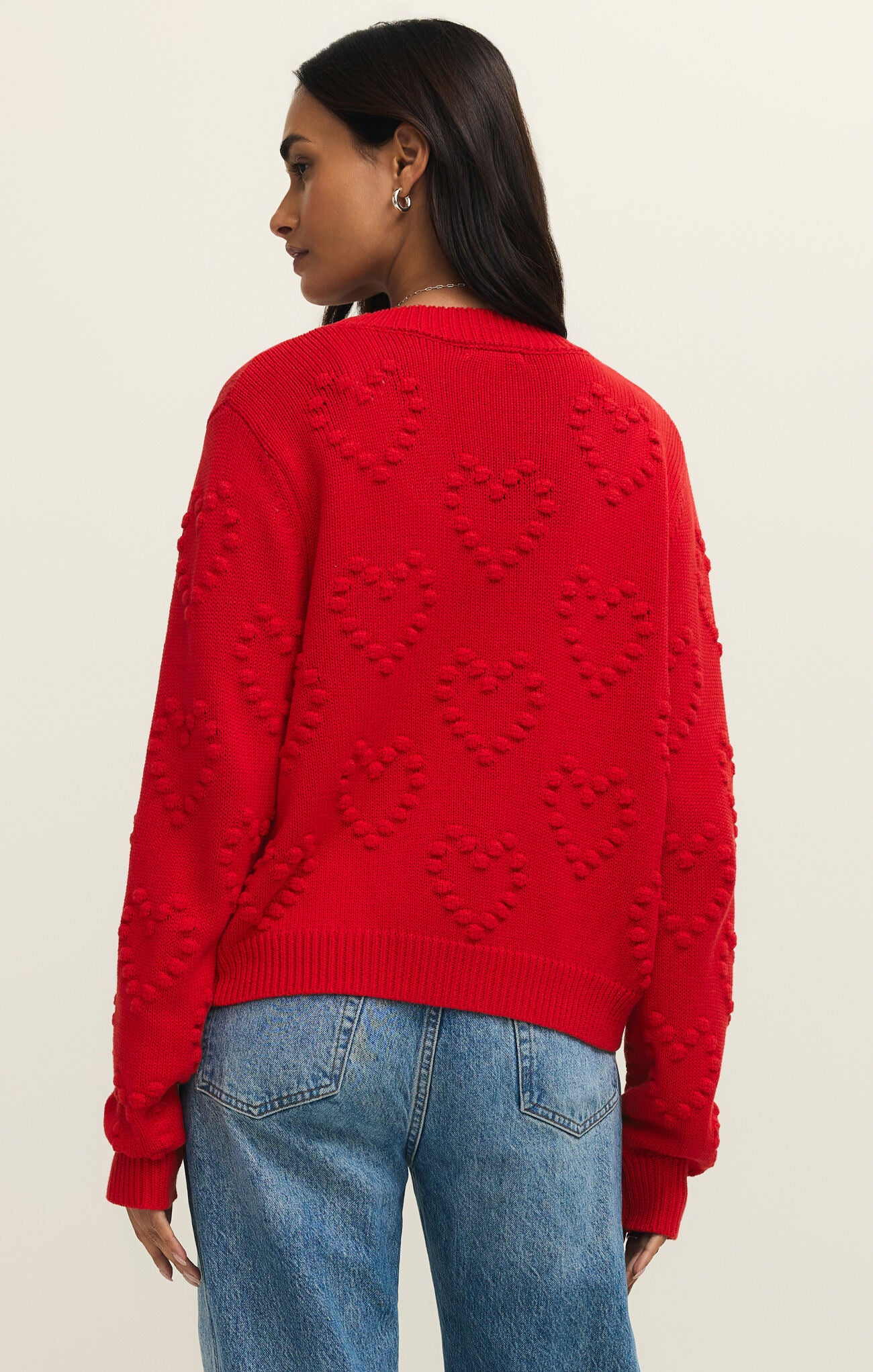 Red knit sweater with raised heart patterns worn with blue denim jeans, shown from the back.