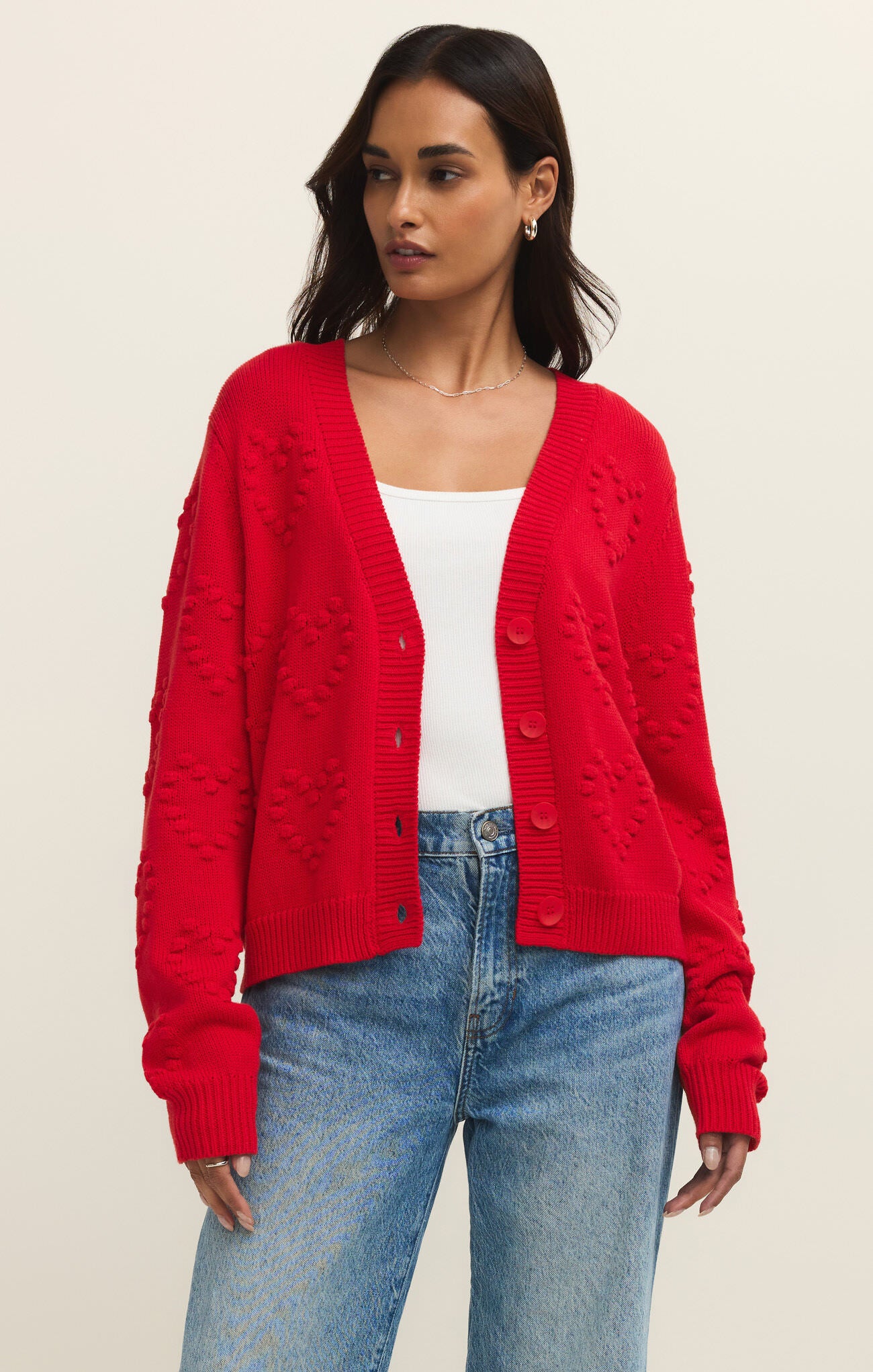 Model wearing a red Z Supply All Yours Heart Cardigan with heart patterns, paired with denim jeans and white top