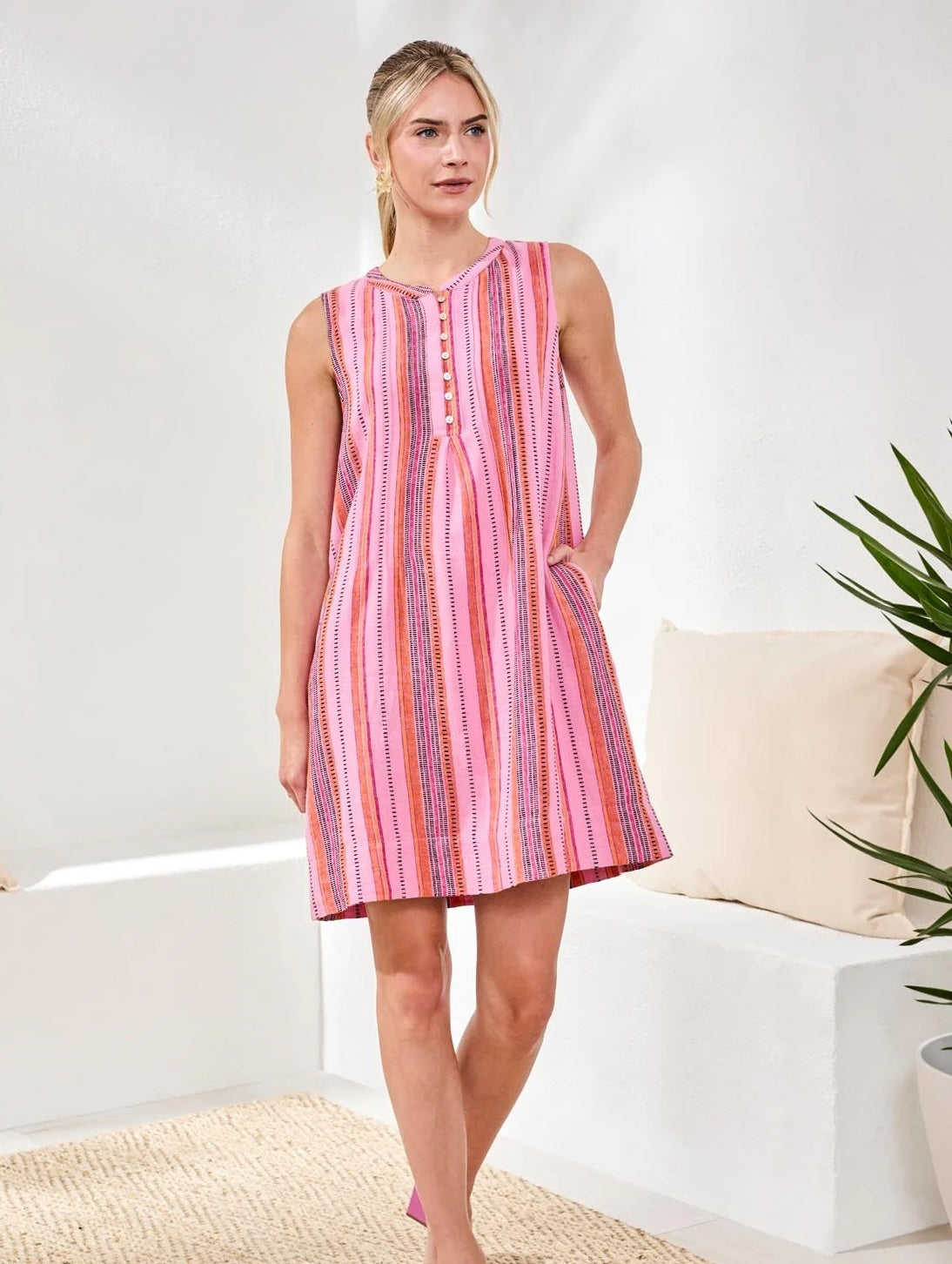 Sleeveless dress with vertical stripes in pink and purple hues featuring pintuck and button details in a light, airy setting.